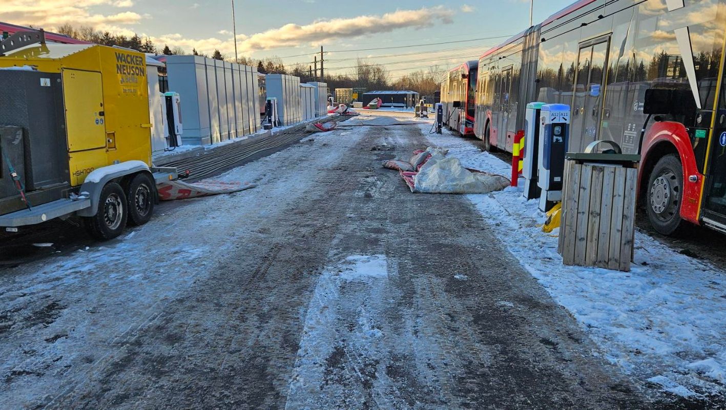 Busser står parkert ved ladestasjoner i snødekt område med gule tekniske enheter